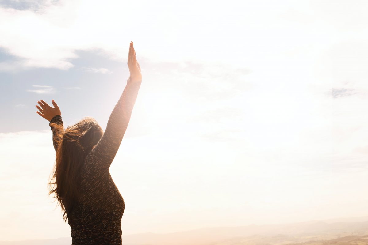 Woman raising hands above head with sun shining in background