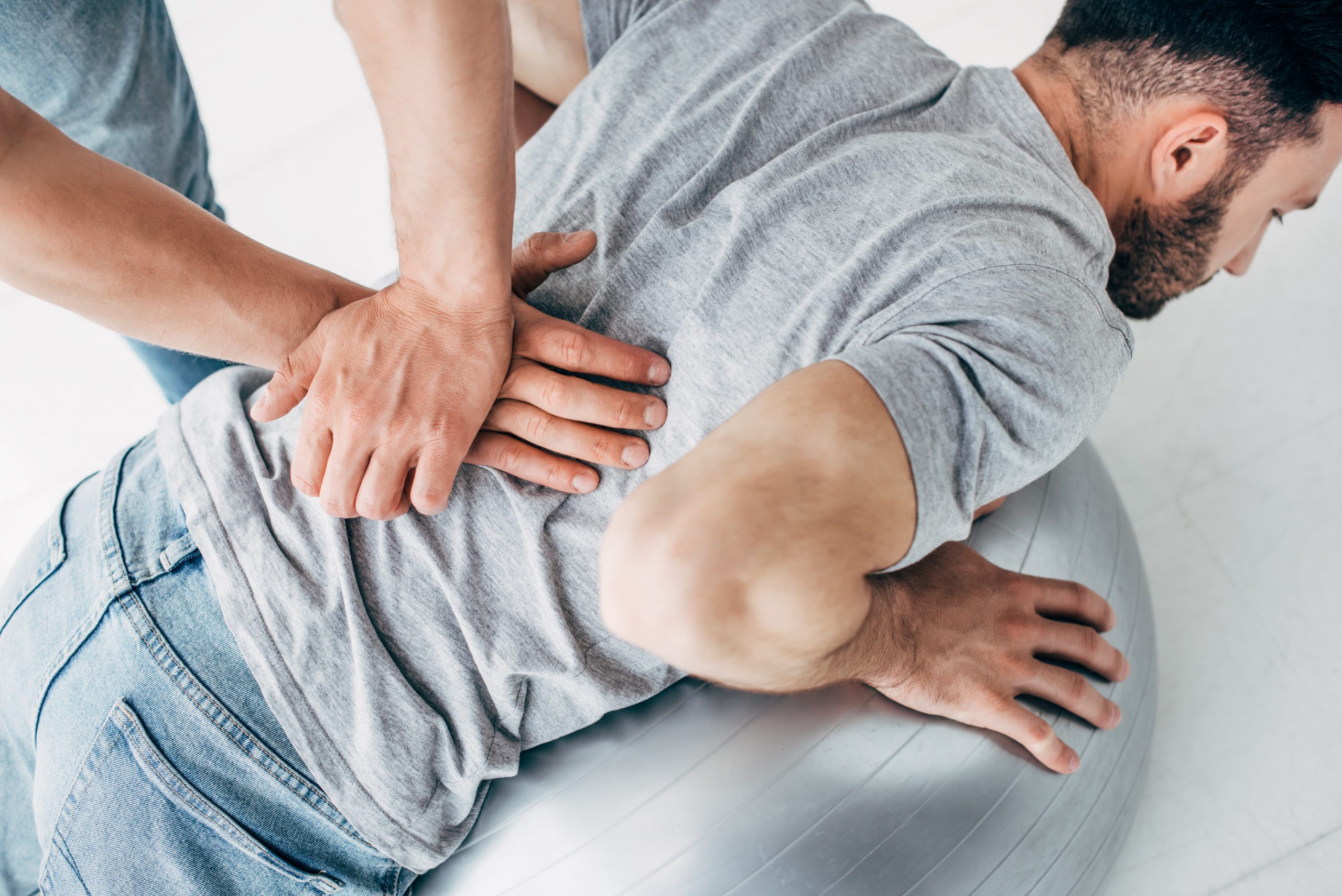 chiropractor treating back pain on man lying on a medicine ball