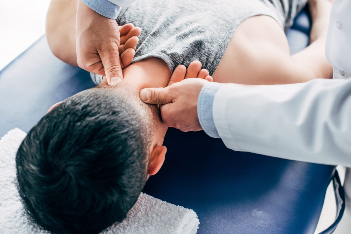 patient lying face down on table while chiropractor adjusts his neck
