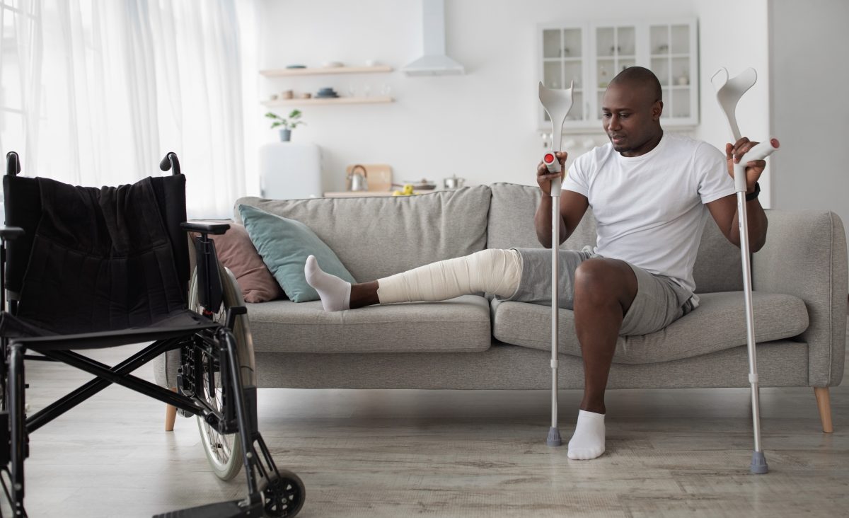 man sitting on couch with bandaged knee holding crutches