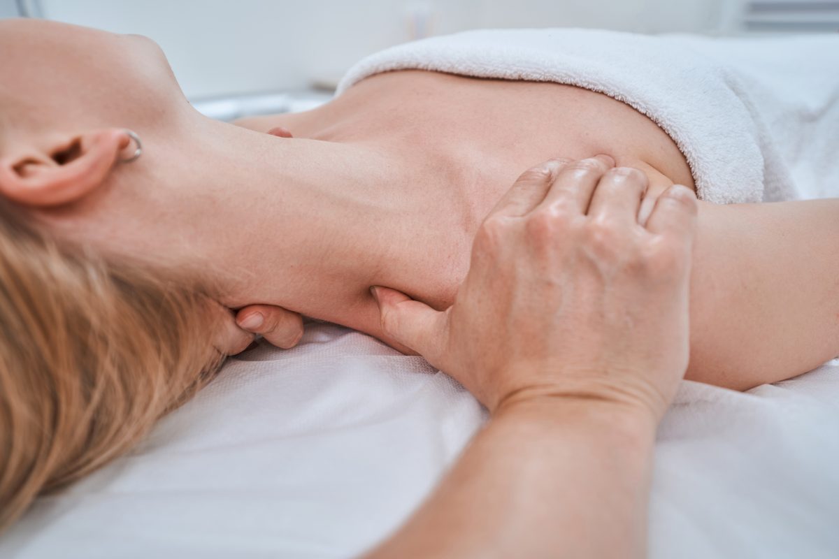Cropped photo of a blonde Caucasian woman lying supine during the trigger point massage performed by a physiotherapist