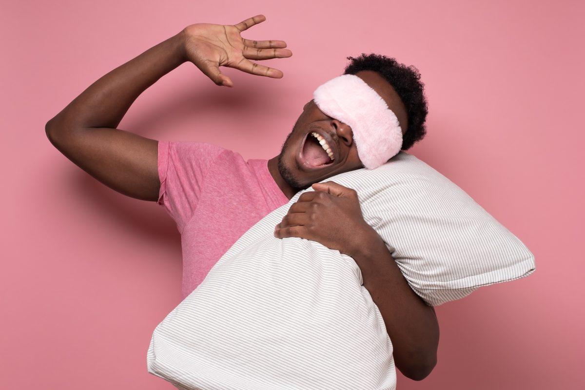 man holding pillow and wearing a sleep mask