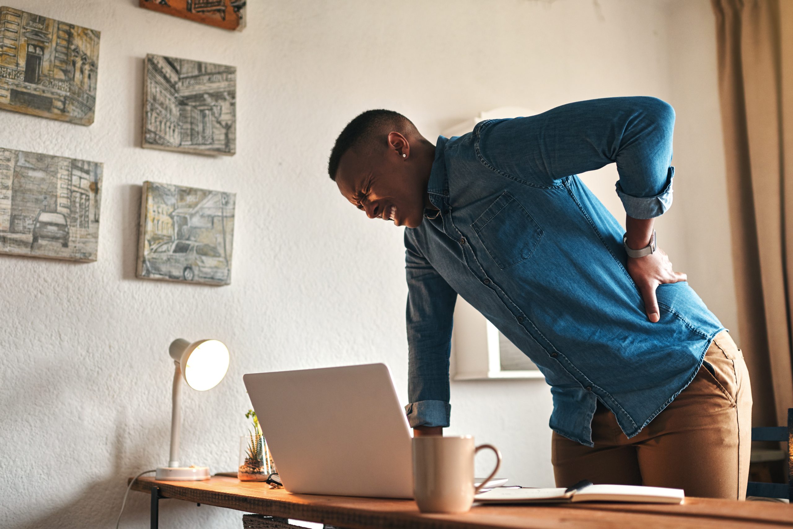man leaning on desk while holding back in pain