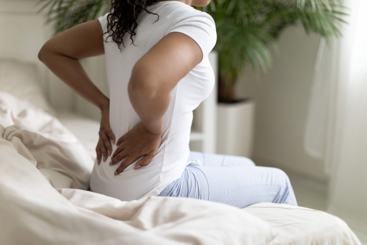 woman sitting on bed and holding lower back in pain