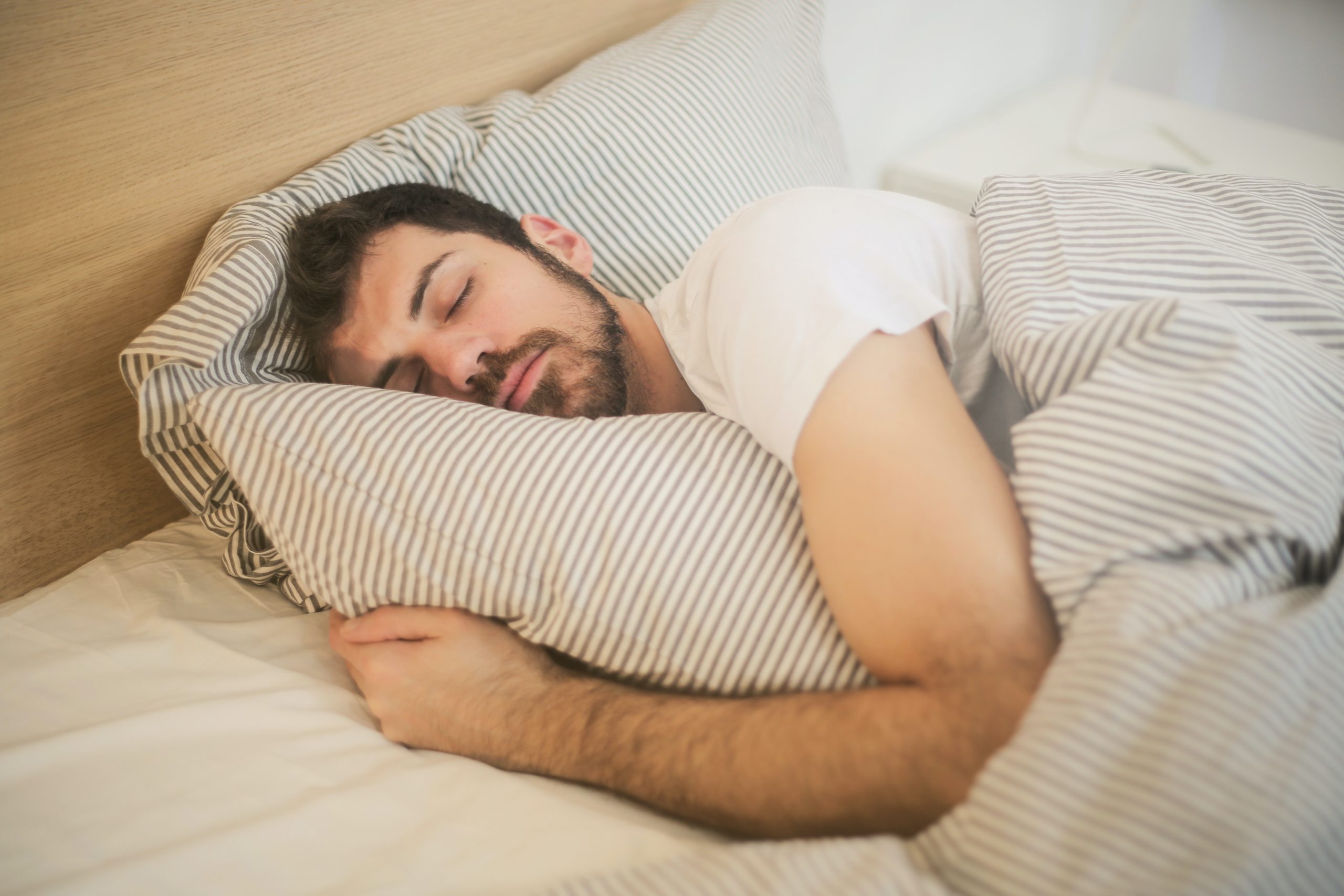 Man sleeping in bed with arm wrapped around pillow